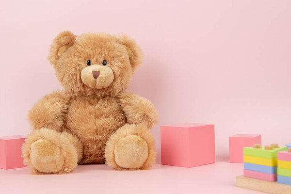 Детские игрушки фон. Образовательные деревянные игрушки и плюшевый мишка на розовом фоне. Вид спереди.