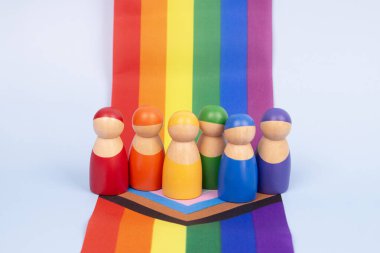 Canlı LGBTQ gökkuşağı bayrağının üzerinde duran renkli ahşap insan figürleri. Çeşitlilik ve kapsayıcılık kavramı.