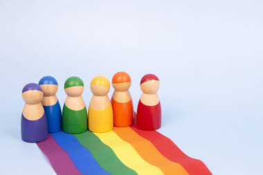 Tahta heykelcikler ve açık mavi arka planda LGBTQ gökkuşağı bayrağı. Çeşitlilik ve kapsayıcılık kavramı.