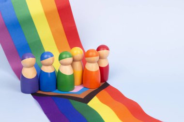 LGBT gururlu ay geçmişi. LGBTQ gökkuşağı bayrağının üzerinde duran küçük tahta insan figürleri. Çeşitlilik ve kapsayıcılık kavramı.
