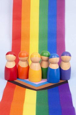 Canlı LGBTQ gökkuşağı bayrağının üzerinde duran renkli ahşap insan figürleri. Çeşitlilik ve kapsayıcılık kavramı.