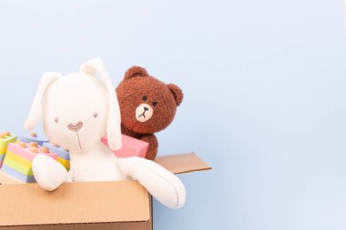 Kahverengi oyuncak ayı, beyaz tavşan ve açık mavi arka planda karton kutuda eğitici tahta oyuncaklar. Çocuklu fakir aileler için bağış kutusu..