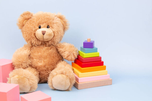 Детские игрушки фон. Медведь Тедди, укладка пирамиды и розовые кубики на голубом фоне. Монтессори образовательные игрушки для детей. Вид спереди.