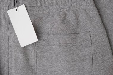 Gri koşucuların üzerinde beyaz kağıt etiket var. Yeni kıyafetlere asılı fiyat etiketi modeli. Üst görünüm.