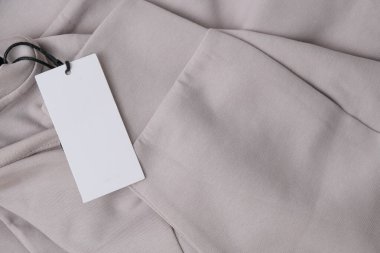 Yeni bej renkli spor kıyafetlere boş beyaz kağıt askı etiketi. Dikdörtgen beyaz etiket modelinin üst görünümü.