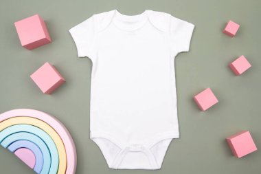 Beyaz pamuklu bebek, yeşil arka planda koruyucu kıyafet ve sürdürülebilir tahta eğitici oyuncaklar yetiştiriyor. Bebek ve kızlar için uygun yeni doğan bebek tulumunun maketi. Üst görünüm.