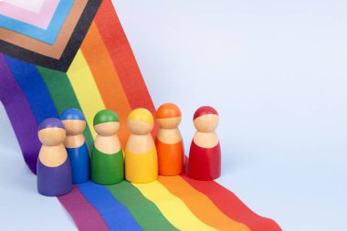 LGBT gururlu ay geçmişi. LGBTQ gelişim bayrağında duran küçük ahşap insan figürleri. Çeşitlilik ve kapsayıcılık kavramı.