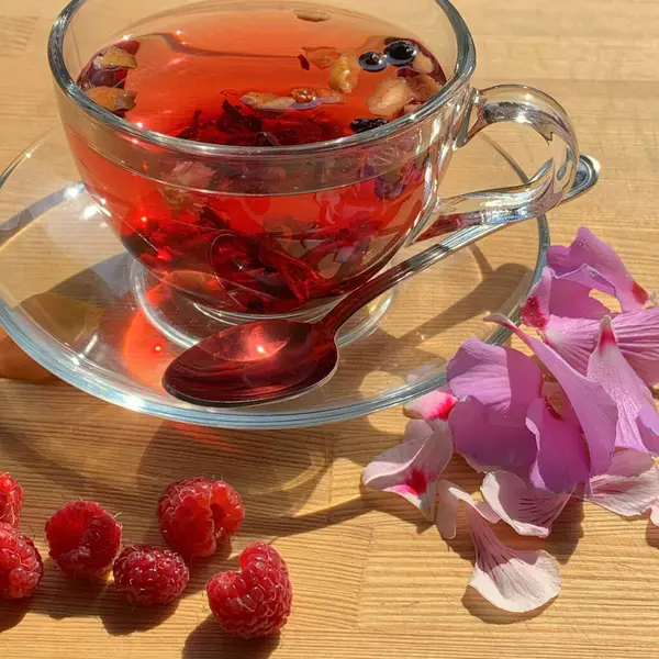 A cup of berry tea on a wooden table with flower petals and raspberries