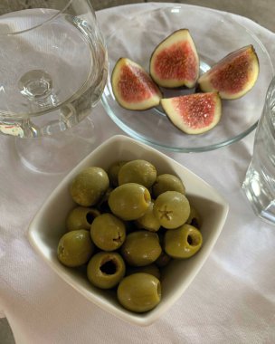 İçkili bir bardak, yeşil zeytin ve beyaz arka planda incir.
