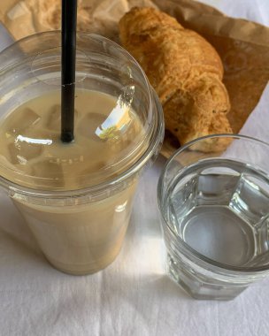 Buzlu latte, kruvasan ve beyaz masa üzerinde bir bardak su.