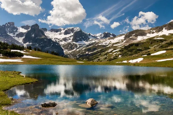 Karla kaplı tepeleri, dağlık çayırları ve etrafındaki tepeleri yansıtan kristal berrak dağ gölleriyle çarpıcı bir dağ manzarası.