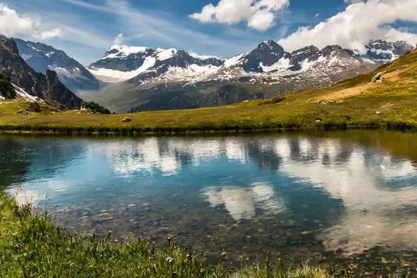 Karla kaplı tepeleri, dağlık çayırları ve etrafındaki tepeleri yansıtan kristal berrak dağ gölleriyle çarpıcı bir dağ manzarası.