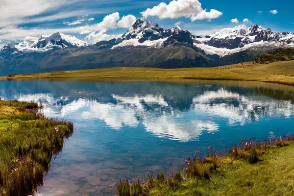 Karla kaplı tepeleri, dağlık çayırları ve etrafındaki tepeleri yansıtan kristal berrak dağ gölleriyle çarpıcı bir dağ manzarası.