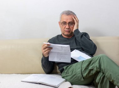 Kağıt dökümanlarda beklenmedik haberler okuyan orta yaşlı bir adam. Şaşırmış ve şaşırmış durumda: yüksek fatura faturası, borç bildirimi, kötü mali rapor, para sorunu