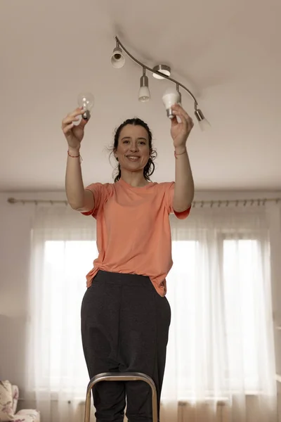 Power saving concept. Smiling woman changing  incandescent lamp with energy saving light bulb
