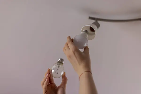 Power saving concept. Woman changing  incandescent lamp with energy saving light bulb