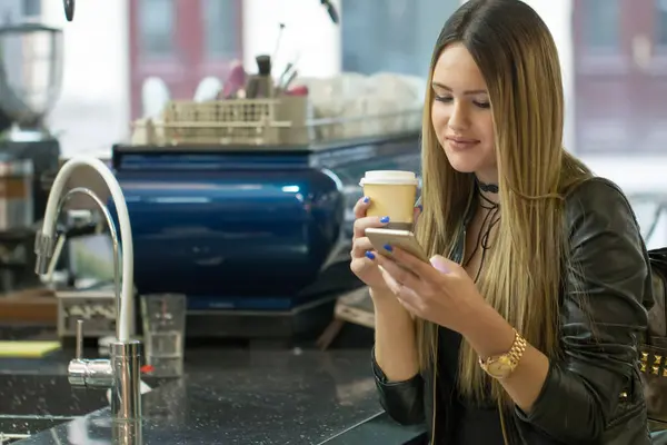 Kadın telefonu kafede söz görüntüsü. Bir kafede otururken ve cep telefonu kullanarak genç güzel kız