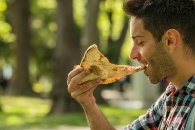 Sokakta pizza yiyen yakışıklı bir genç adam var. Pizza zamanı. Öğrenci öğle yemeği molasında..  
