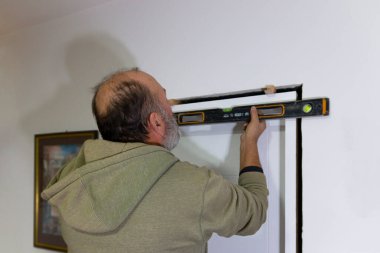 Kapı çerçevesine karşı ruh seviyesinde çalışan bir işçinin elleri. Tecrübeli bir marangoz yeni daireye ahşap çerçeveli iç kapı kuruyor.. 