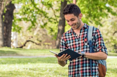 Kitabı olan bir üniversite öğrencisi. Parkta ödev yapan öğrenci..