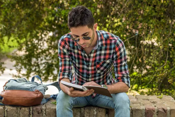 Kitabı olan bir üniversite öğrencisi. Parkta ödev yapan öğrenci..