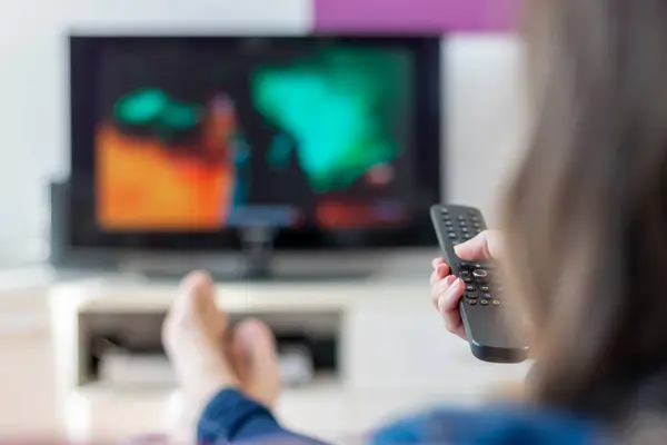 Kız kanepede dinleniyor ve uzaktan kumandanın yardımıyla televizyondaki programlara bakıyor. Etkinlik yaşam tarzları konsepti