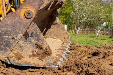 Özel bir araziyi temizleme ve yerle bir etme. Sarı kazıcı toprağı geniş bir kovada götürüyor.