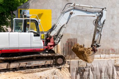 Ekskavatör şantiyede toprak ile bir damperli kamyon dolduruyor, proje devam ediyor.