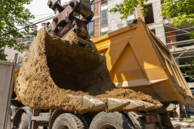 Büyük kazıcı bir çöp kamyonunu inşaat alanında toprakla dolduruyor..