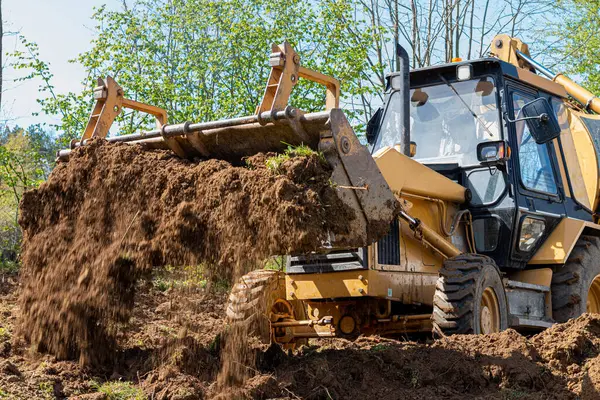Özel bir araziyi temizleme ve yerle bir etme. Sarı kazıcı toprağı geniş bir kovada götürüyor.