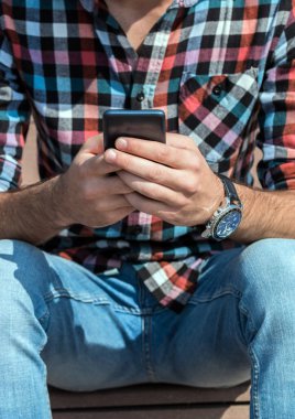 Modern adamın portresi merdivenlerde oturuyor, akıllı telefon kullanıyor. Hafta sonu için plan yapıyorum..