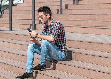 Modern adamın portresi merdivenlerde oturuyor, akıllı telefon kullanıyor. Hafta sonu için plan yapıyorum..