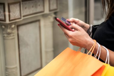 Akıllı telefon tutan ve alışveriş yaparken alışveriş torbası kullanan bir kadın.
