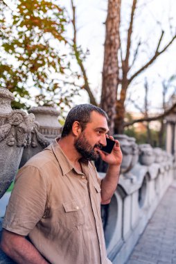 Orta yetişkin sakallı adam konuşurken onun akıllı telefon kullanarak şehrin sokaklarında