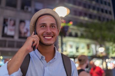 Şapka ve Sırt Çantası ile Yakışıklı Genç Adam City Street Ayakta ve Onun Cep Telefonu üzerinden Talking