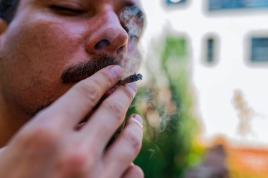 Bir adam elinde bir eklem esrar ot Içiyor. Tıbbi esrar kullanımı ve esrar yasallaştırma kavramları.
