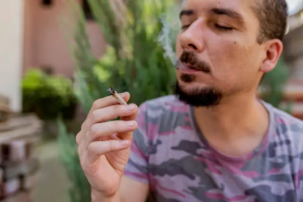 Bir adam elinde bir eklem esrar ot Içiyor. Tıbbi esrar kullanımı ve esrar yasallaştırma kavramları.