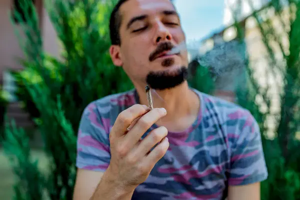 Bir adam elinde bir eklem esrar ot Içiyor. Tıbbi esrar kullanımı ve esrar yasallaştırma kavramları.
