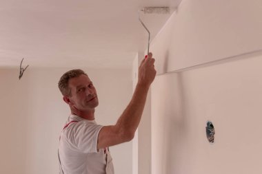 Duvar ve tavan onarımı ve boyaması. Boya, profesyonel bir işçi tarafından duvara uygulanır. Erkek tamirci evin tavanını yuvarlak beyazla boyuyor.. 