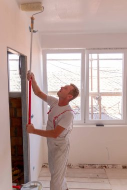 Duvar ve tavan onarımı ve boyaması. Boya, profesyonel bir işçi tarafından duvara uygulanır. Erkek tamirci evin tavanını yuvarlak beyazla boyuyor.. 