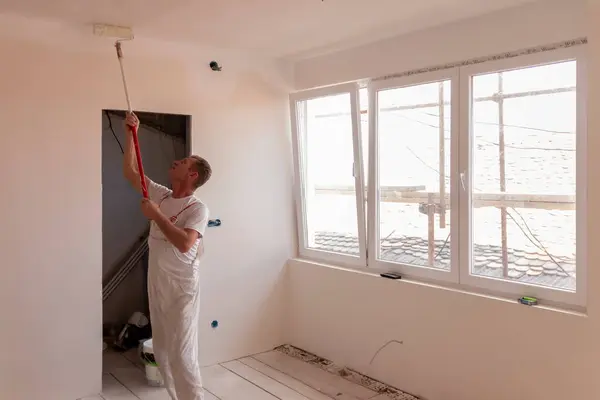 Wall and ceiling repair and painting. Paint is applied to the wall by a professional worker. Male repairman painter paints the ceiling of a house with a roller white.