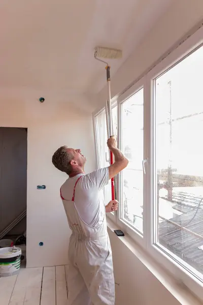 Wall and ceiling repair and painting. Paint is applied to the wall by a professional worker. Male repairman painter paints the ceiling of a house with a roller white.