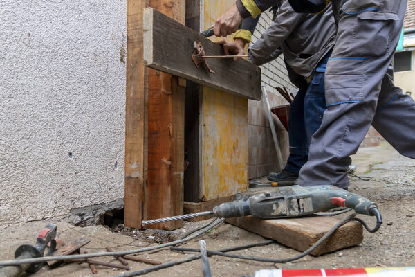 Worker is installing and assembling column formworks for concrete filling at building site. Wooden column formwork secured to masonry using studs. Construction technologies.
