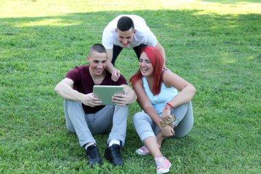 Tablet ve cep telefonları ile halka açık parkta eğlenen bir grup öğrenci