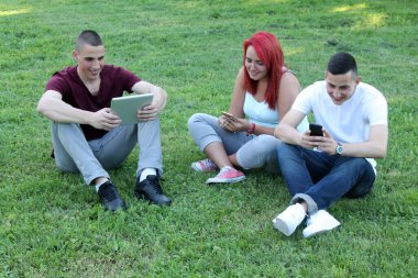 Tablet ve cep telefonları ile halka açık parkta eğlenen bir grup öğrenci