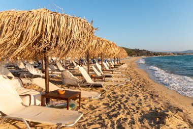 Güneşli yatakları ve şemsiyeleri olan güzel kumlu bir sahil. Tropikal bir yerde gün