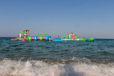 Ormos Panagias, Greece, August 5. 2022: Inflatable bouncing castle drifting on waves of Aegean Sea. Aquapark with attractions in the sea. Popular tourist activity,water sport