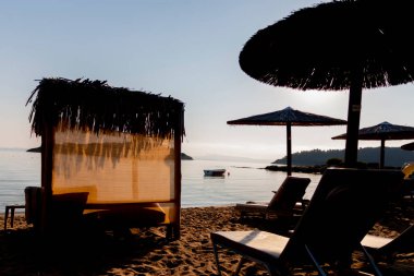 Şafak vakti kumsalda hasır şemsiyeler ve güneşlikler denizin arka planına karşı. Rahatlatıcı tesisler. Plajda tatiller.