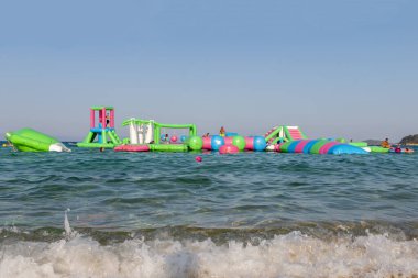 Ormos Panagias, Yunanistan, 5 Ağustos. 2022: Şişme zıplayan kale Ege Denizi 'nin dalgaları üzerinde sürükleniyor. Aquapark 'ın denizdeki cazibesi. - Popüler turizm aktiviteleri, su sporları.