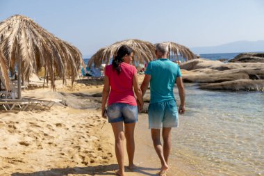 Saf kumsalda çıplak ayakla keyifli bir çift gezintisi. Sahile vuran dalgaların sesi rahatlatıcı bir melodi yaratıyor. Çift kumsalın huzurlu güzelliğinin tadını çıkarıyor..